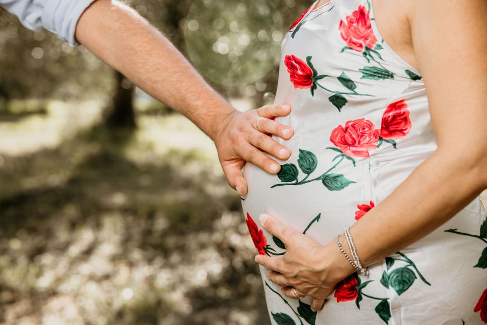 Close-up of couple holding pregnant belly in floral rose maternity dress outdoors.