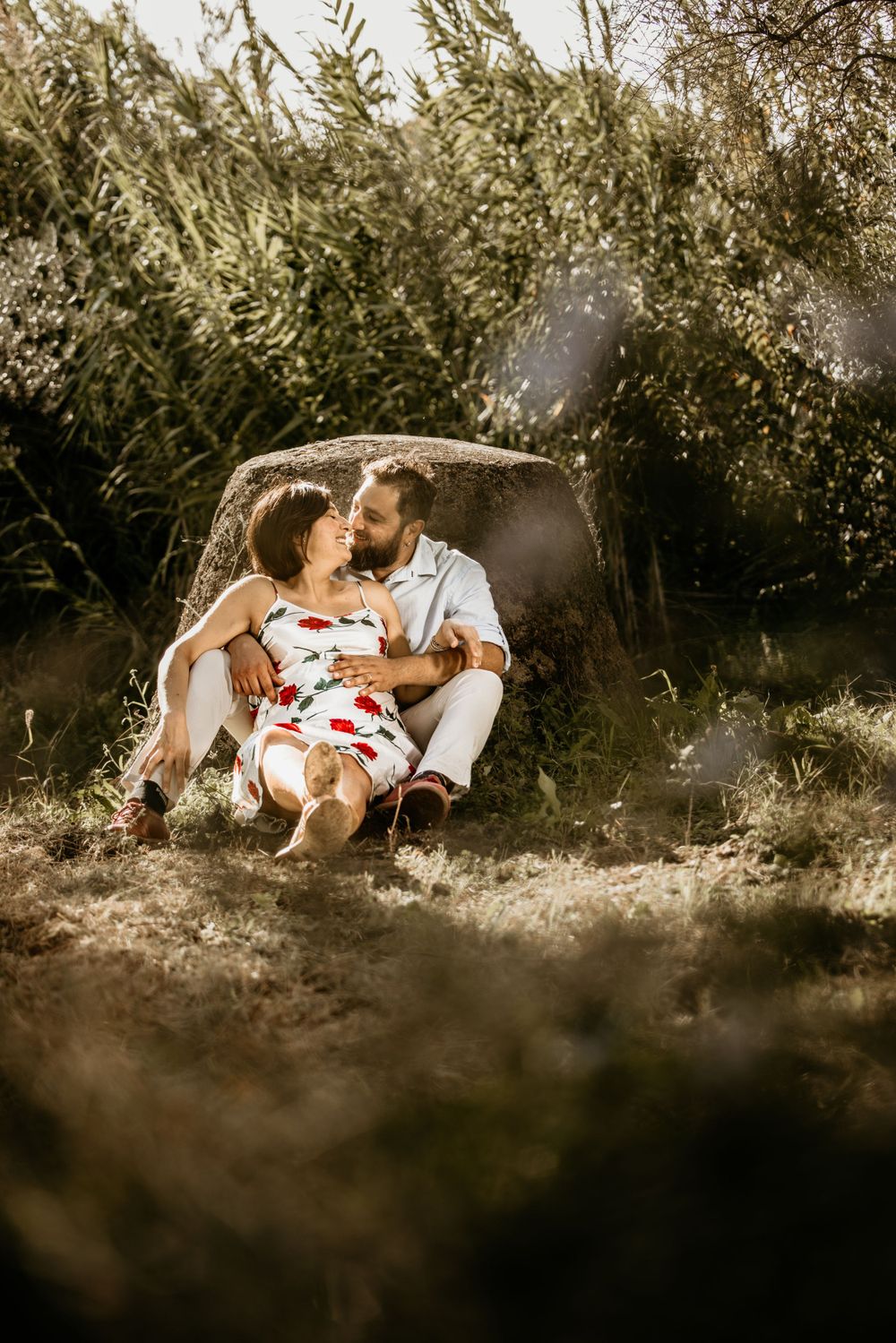 Couple sitting together in a sunny field, sharing a romantic moment during maternity photoshoot.