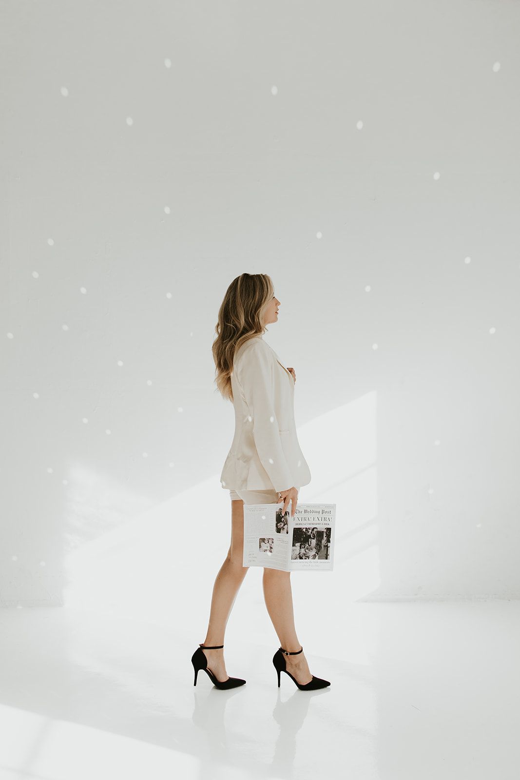 Black and white photo of a bride in a white dress and cowboy boots sitting in a field holding her dog.