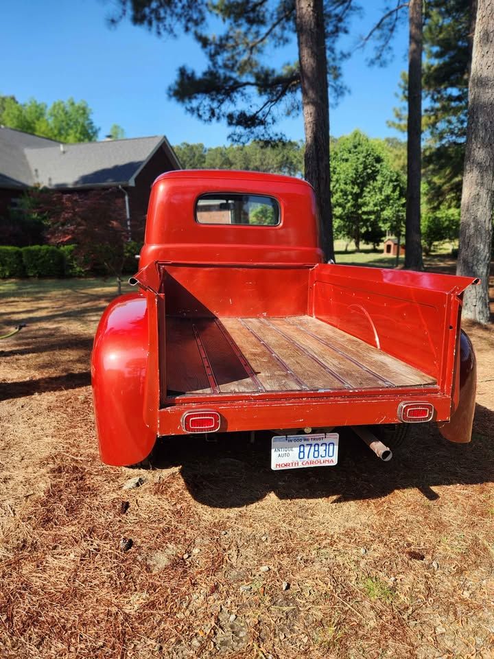 Rear view of a classic red vintage pickup truck with wooden bed floor and South Carolina license plate, parked on pine needles.