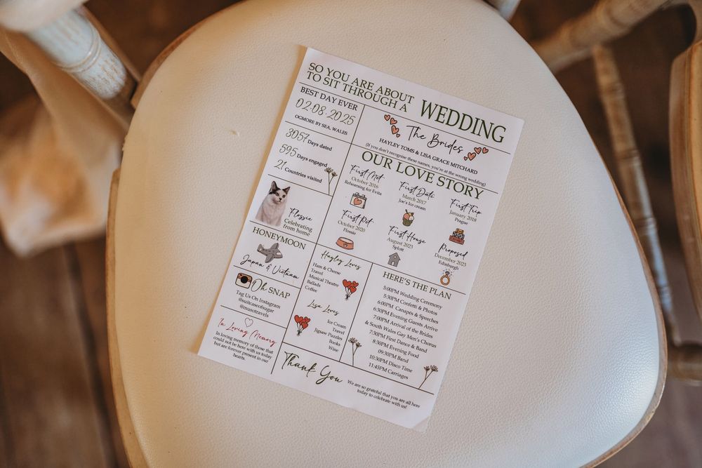 Illustrated wedding program card titled Our Love Story resting on a cream cushioned chair seat at a rustic wedding venue.