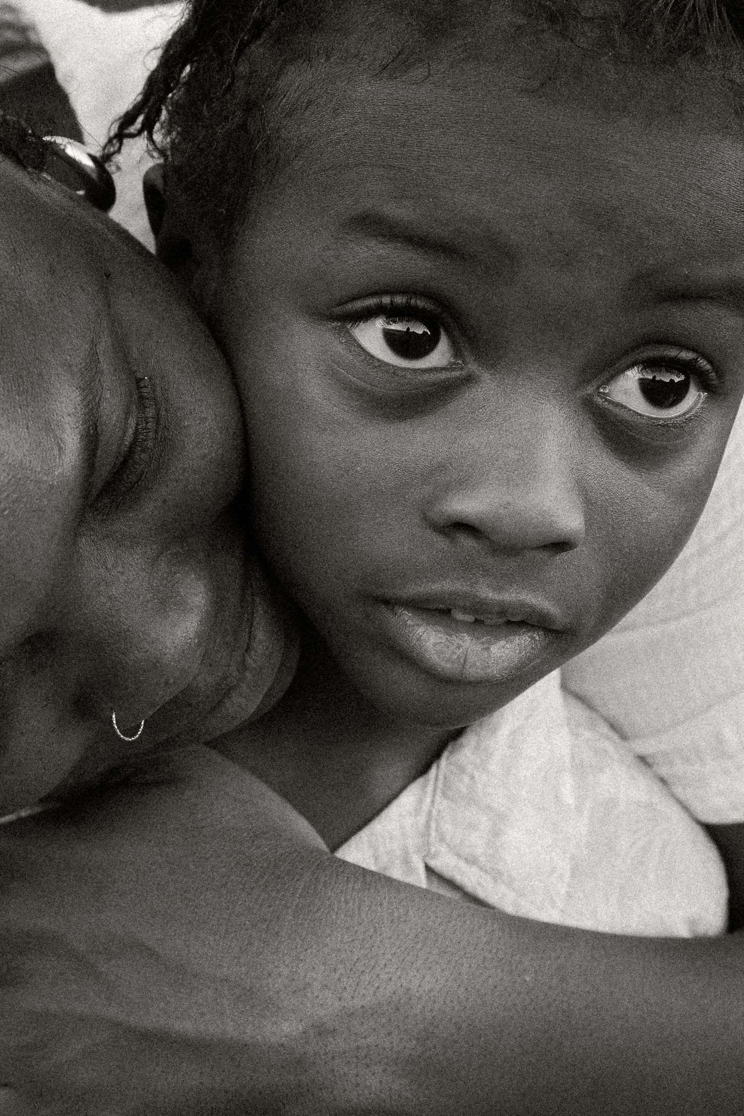 Black and white photo of a young child resting their head on an adults shoulder, gazing at the camera with expressive eyes at Papago Park.