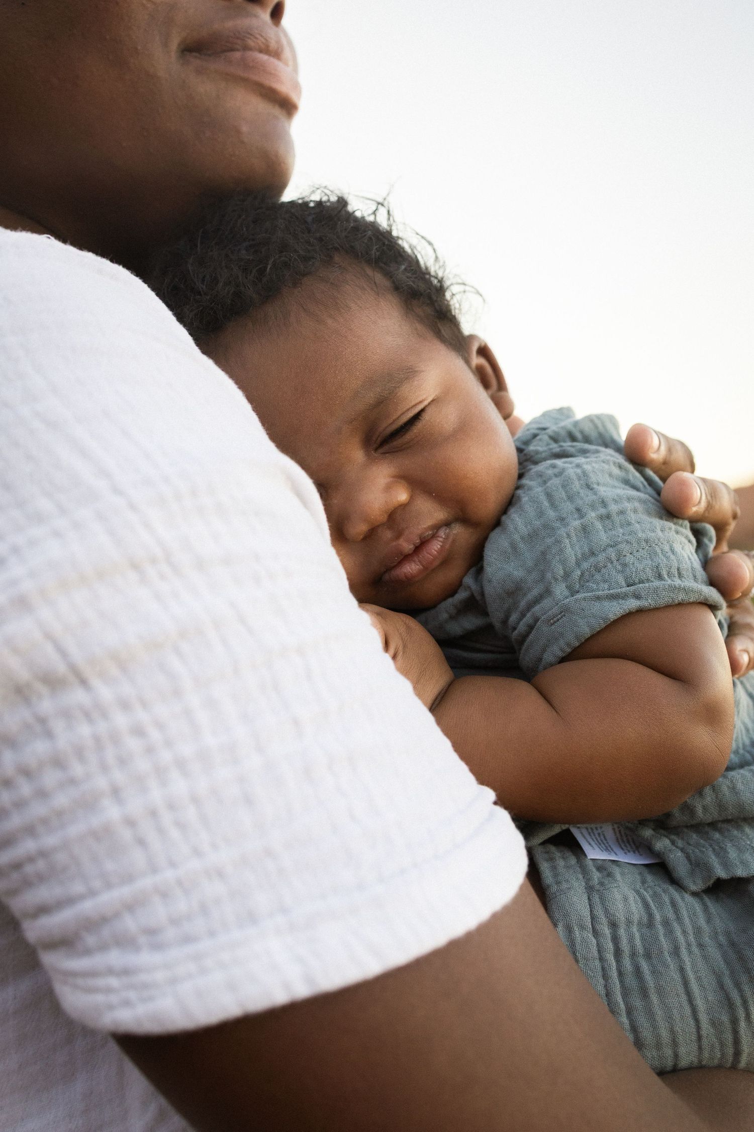 A parent tenderly holds a sleeping newborn baby against their chest outdoors at Papago Park in Phoenix.