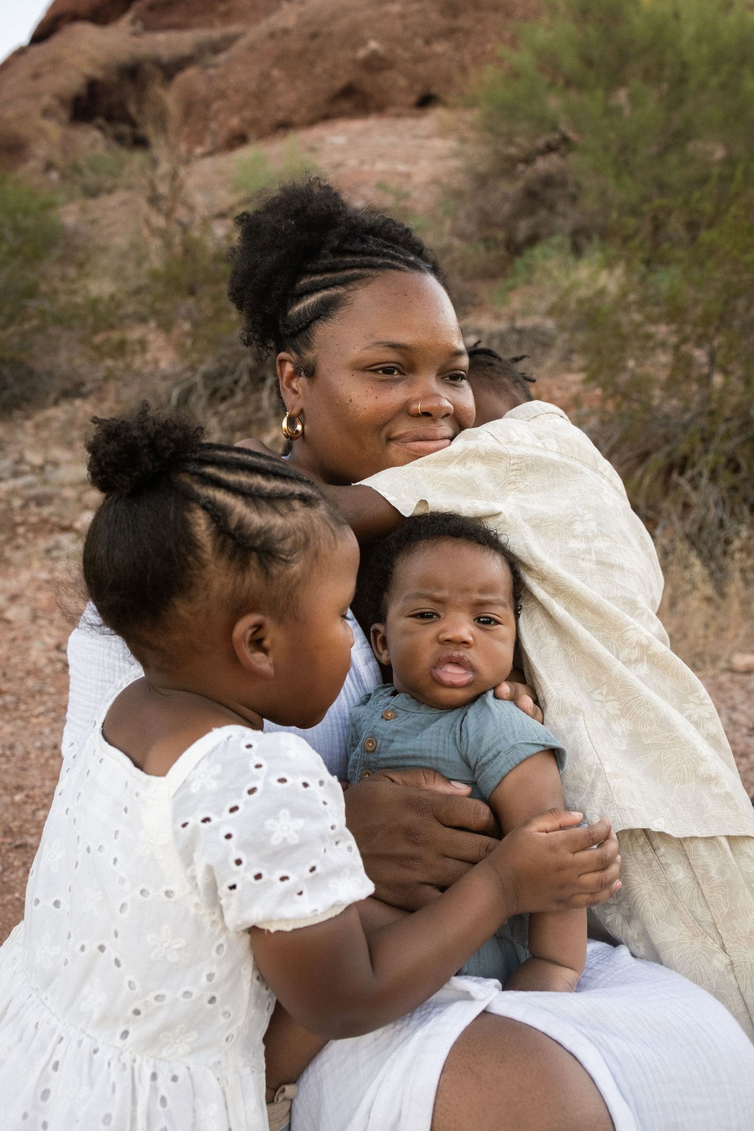 A happy Black mother smiles while holding infant and young daughter at Papago Park in Phoenix.