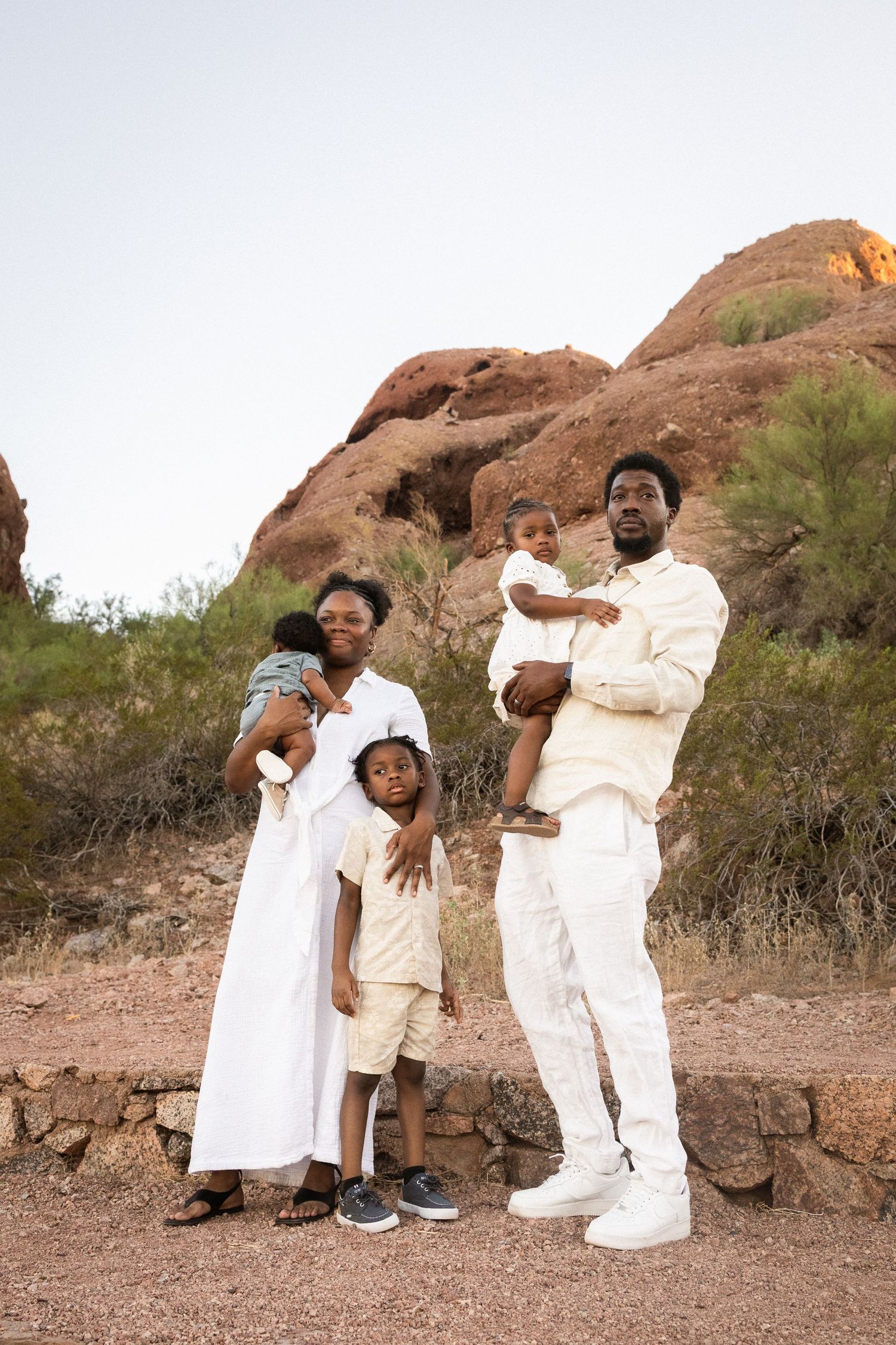 A joyful Black family of five poses together near red rock formations at dusk at Papago Park in Phoenix