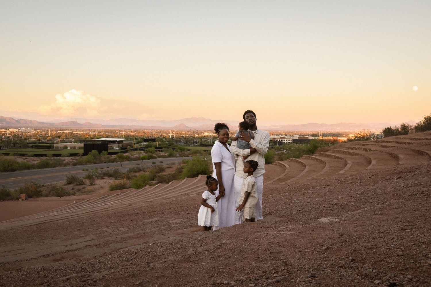 Family of four in white outfits posing on a hillside at sunset with a scenic desert landscape behind them at Papago Park in Phoenix.