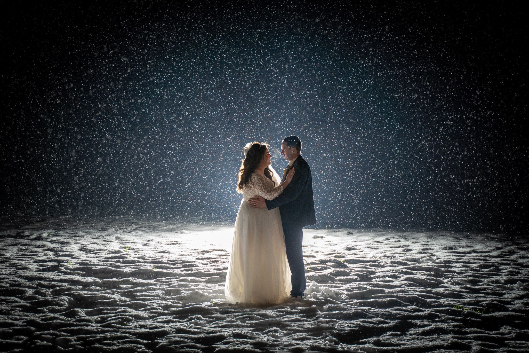 Bride in a white gown and groom embrace in a snowy field at Breaffy house, Mayo. Photo by AK wedding photography and videography.