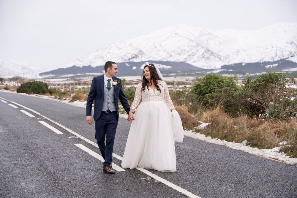 Bride in a white tulle gown and groom walk down a snowy road in Connemara photo by AK wedding photography and videography.
