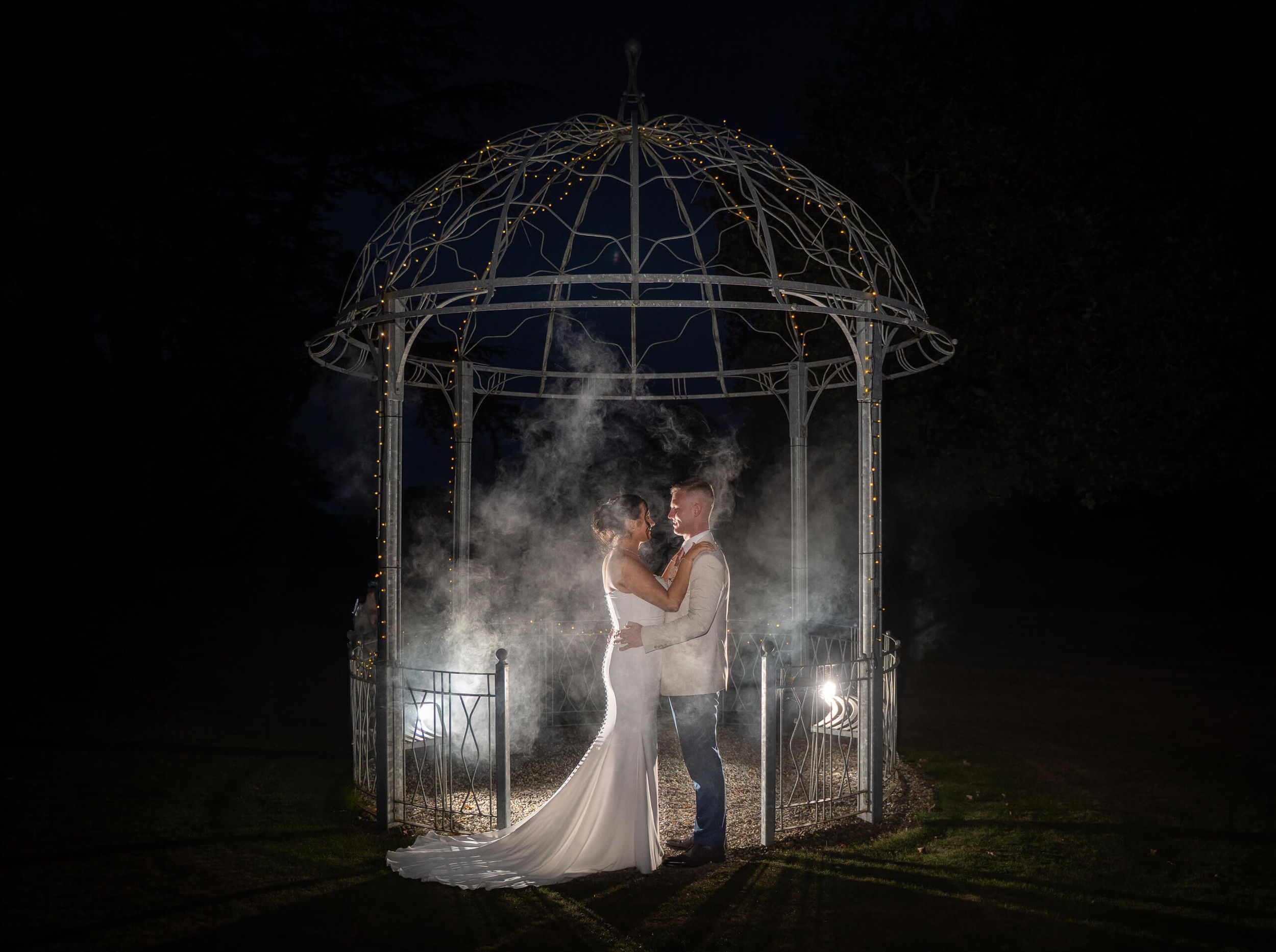 Bride and groom embrace inside a lit wrought-iron gazebo at Ballykealey house county Carlow photo by AK wedding photography and videography.