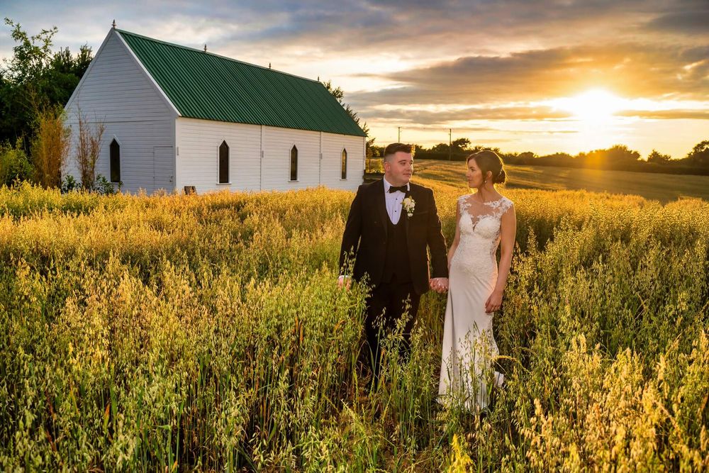 Bride and groom hold hands in a golden wheat field at sunset at the Clanard Court Hotel photo by AK wedding photography and videography.
