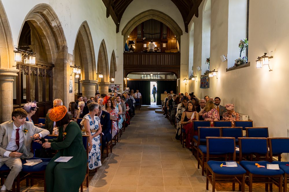Wedding guests seated in historic stone church nave awaiting ceremony with blue chairs and arched columns.