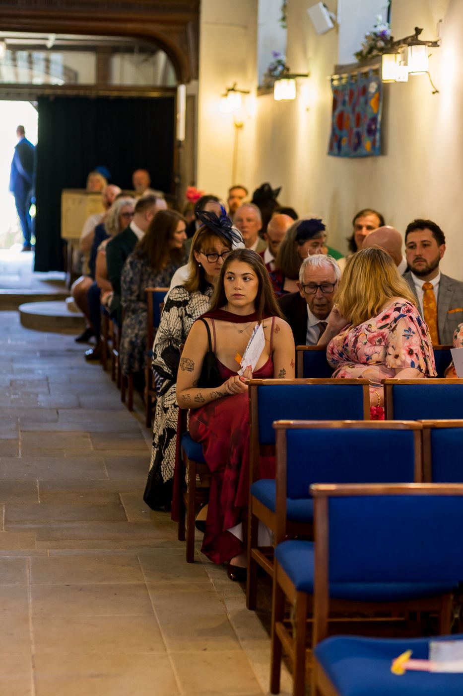 Wedding guests seated in church pews with blue cushions, awaiting the ceremony to begin.