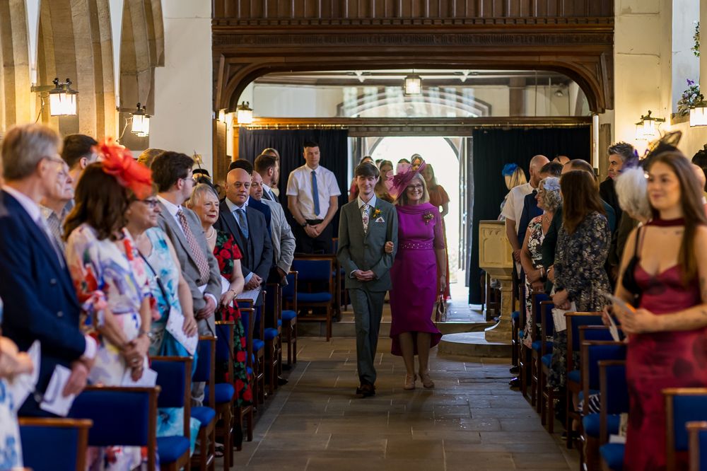 Wedding procession walking down church aisle with guests seated on both sides.