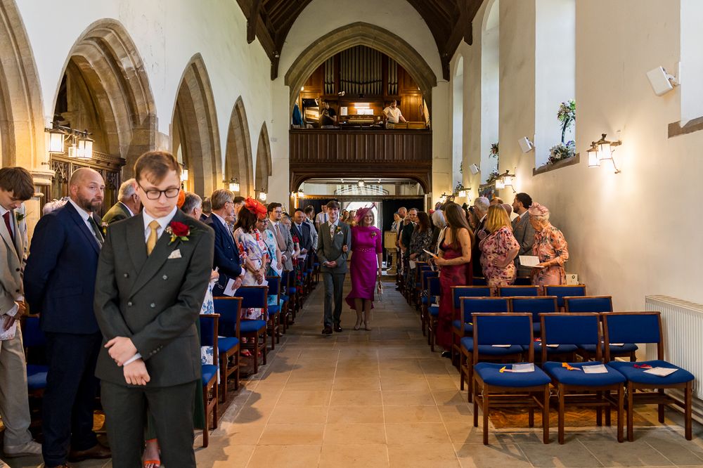 Guests gather in a traditional stone church for a wedding ceremony, with blue chairs lining the aisle.