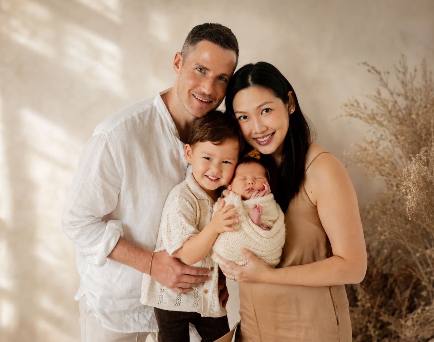 Happy family of four posing for a newborn photo session, parents smiling with toddler holding swaddled baby.