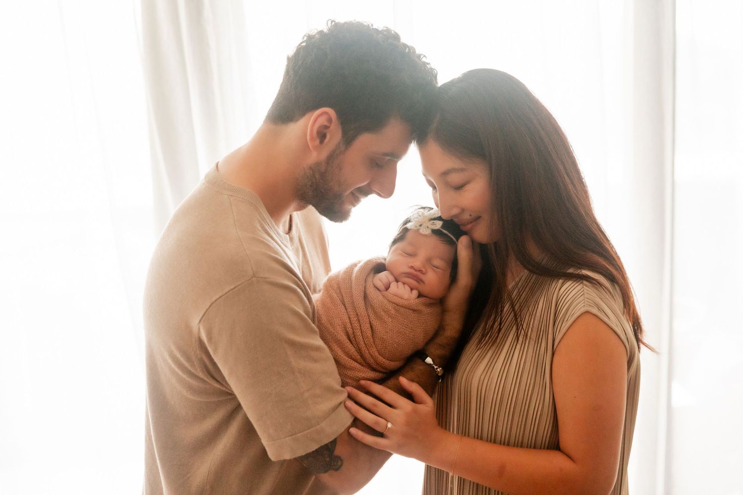 New parents tenderly hold their swaddled newborn baby together, sharing an intimate family moment.