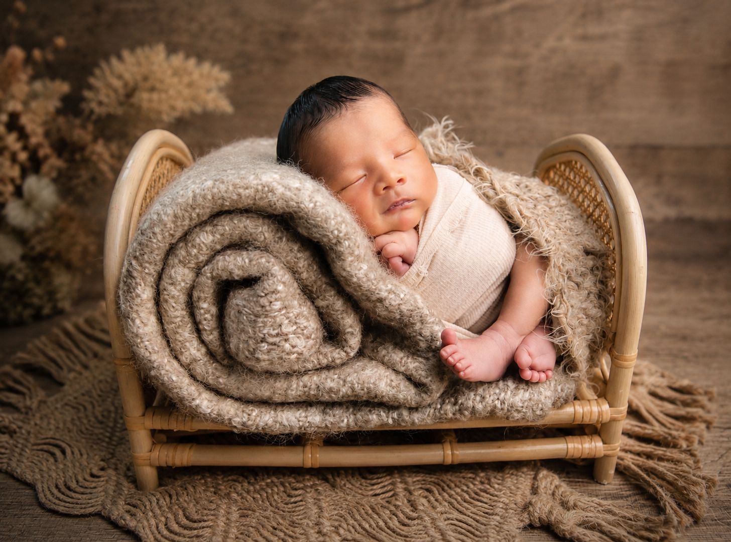 Sleeping newborn baby wrapped in cream swaddle on a cozy knit blanket in a small rustic bamboo bed.