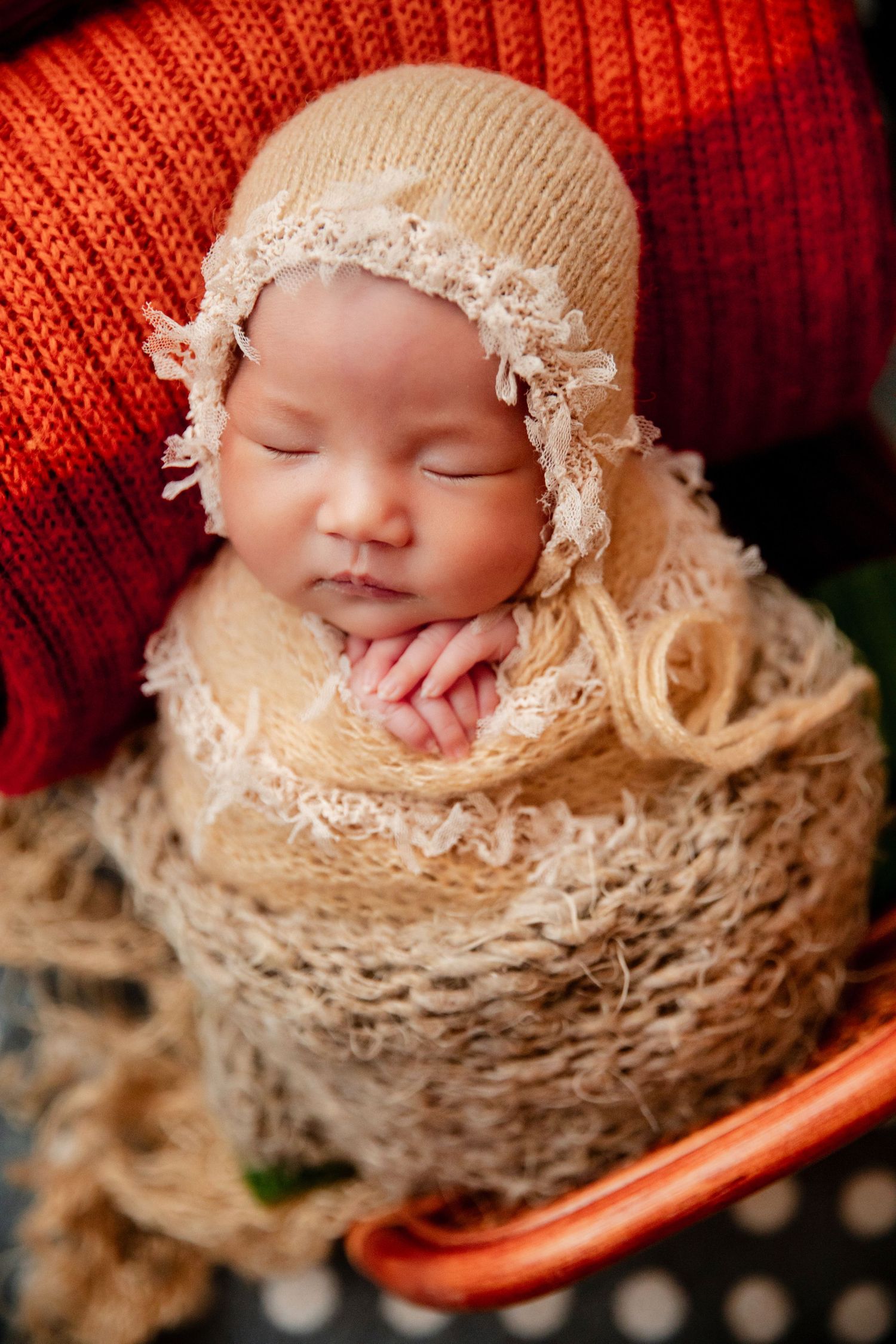 Sleeping newborn baby wrapped in beige knit blanket and bonnet, nestled in a basket.