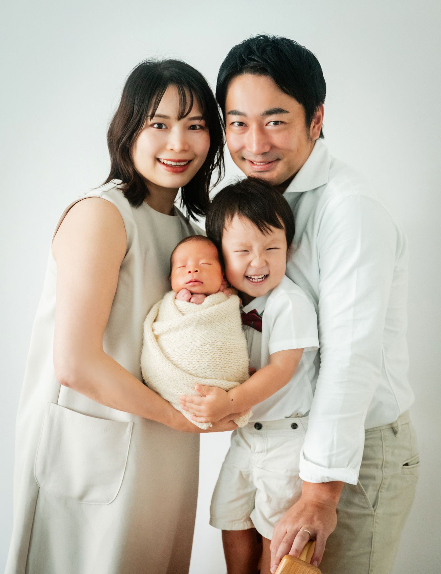 Happy Asian family posing for a studio portrait with a newborn baby and young toddler son.