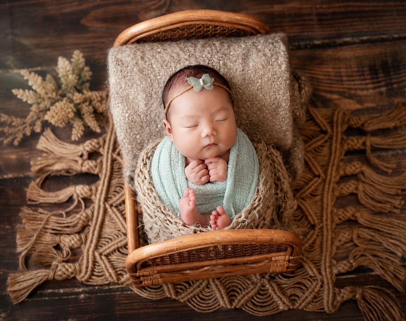 Sleeping newborn baby wrapped in mint green swaddle, resting in a rustic wooden basket with macrame blanket.