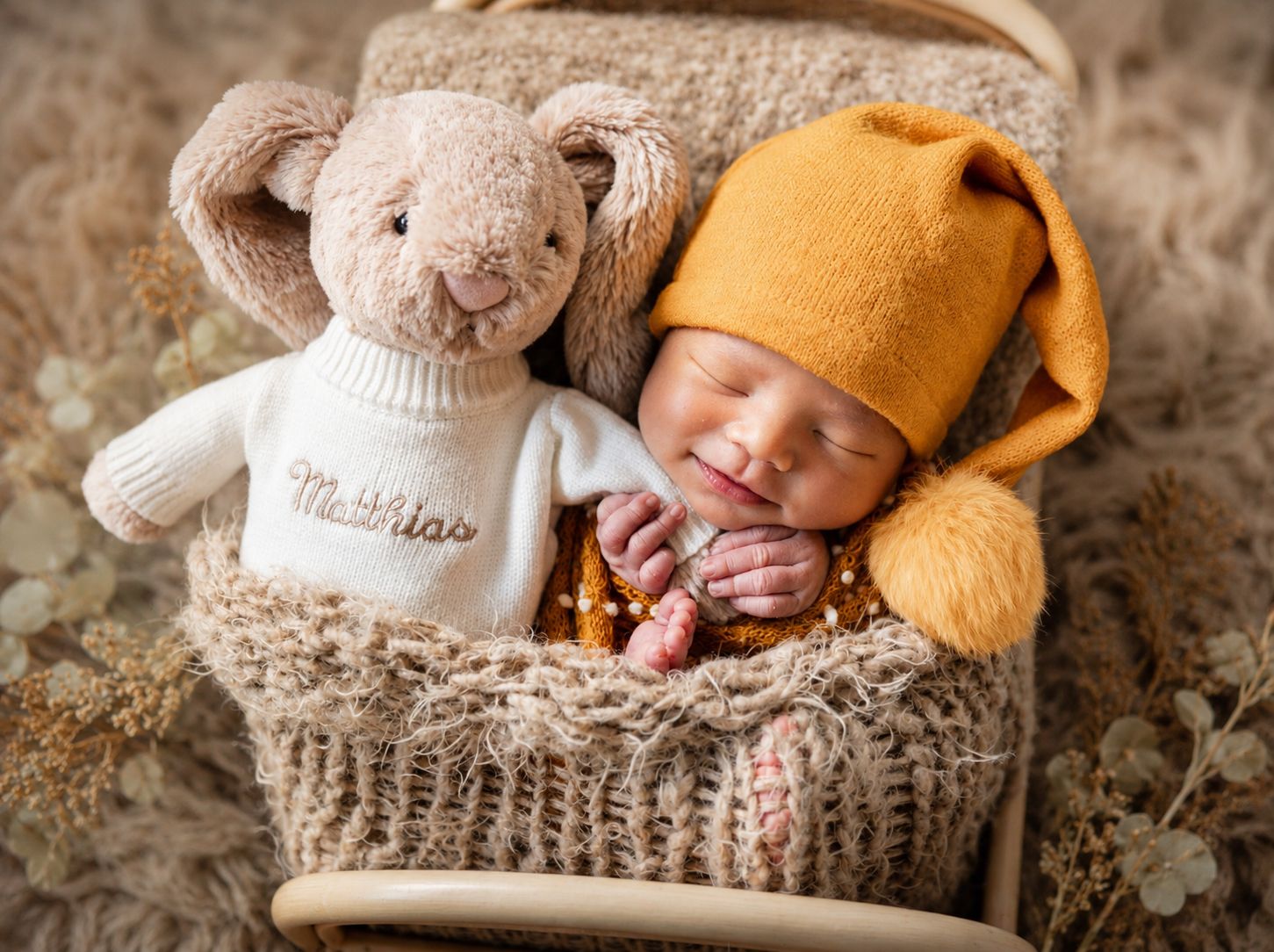 Sleeping newborn baby in mustard knit hat nestled in basket with personalized Matthias stuffed bunny toy.