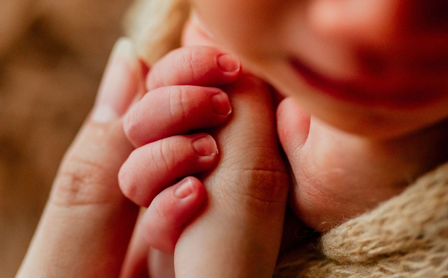 Close-up of a newborn baby's tiny fingers gently grasping an adult's hand, symbolizing new life and parental bond.
