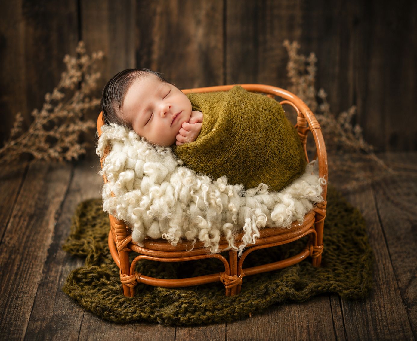 Sleeping newborn baby wrapped in green swaddle smiling in a rustic wicker basket with fluffy white blanket.