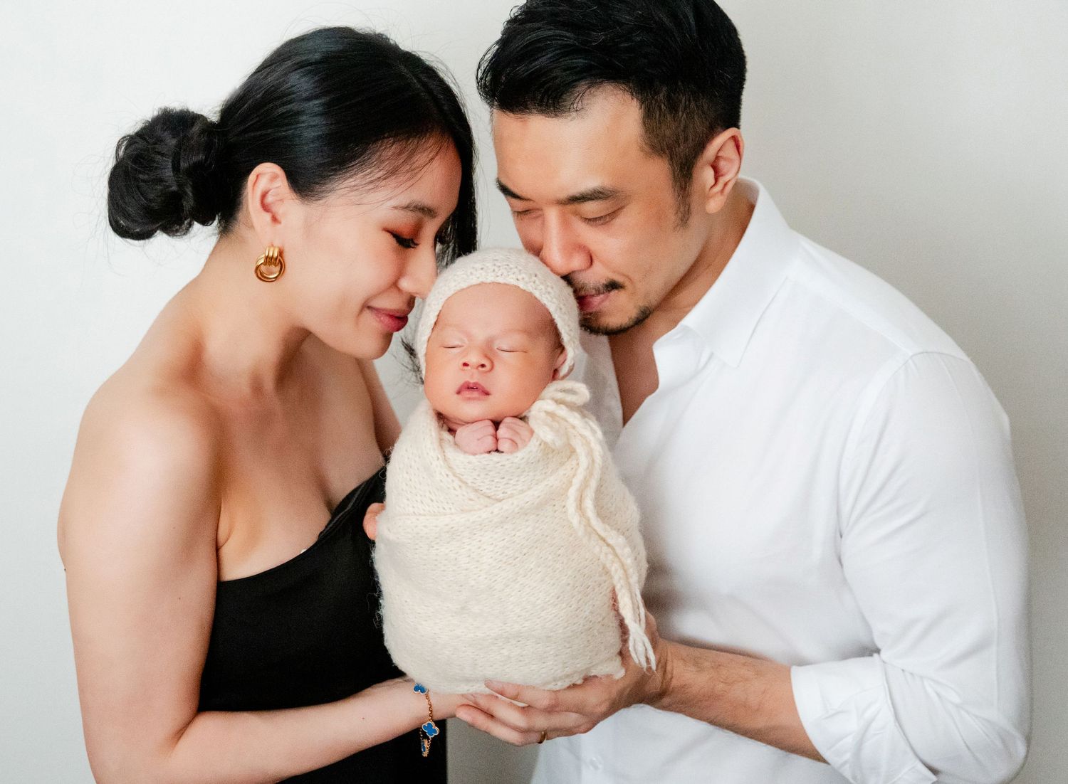 A couple tenderly gazes at their swaddled newborn baby during a professional family portrait session.