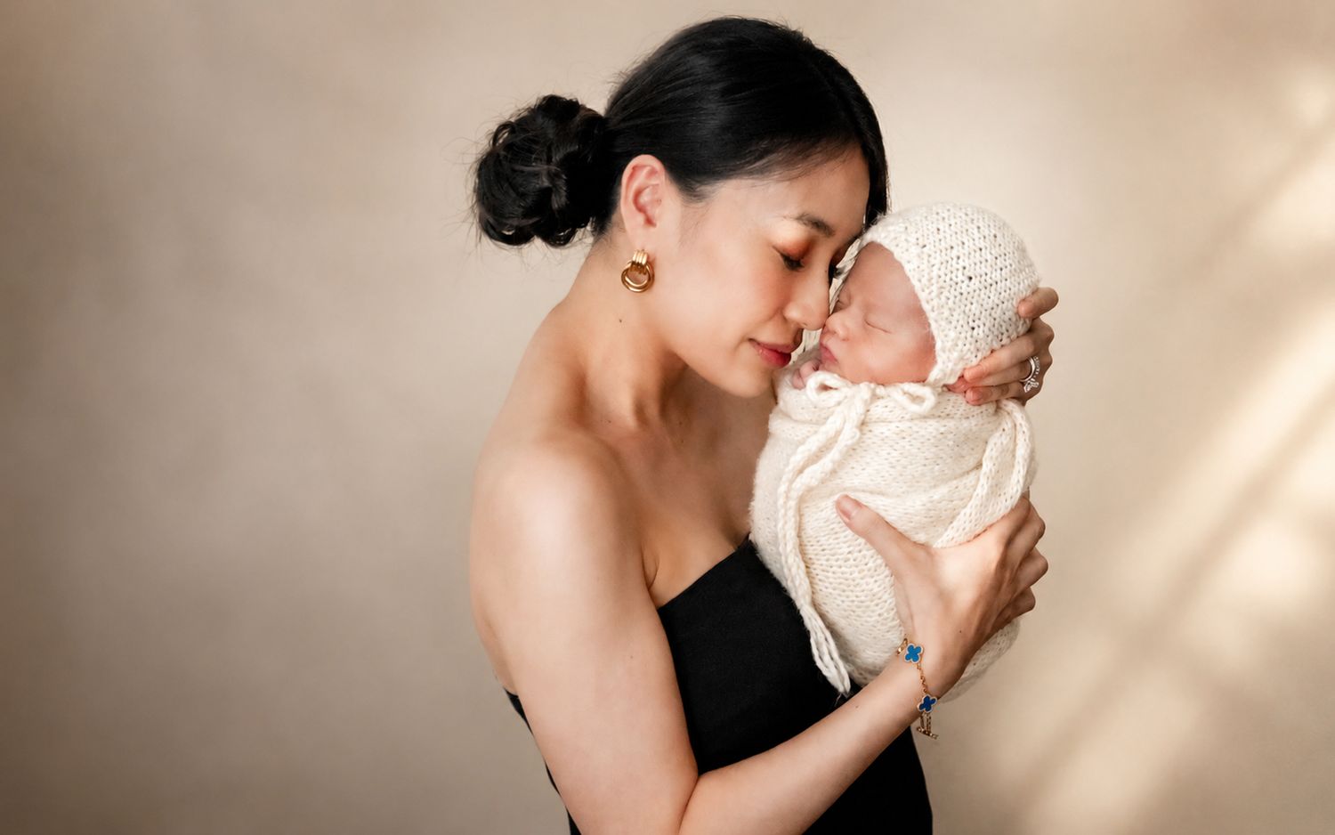 A mother tenderly holds her swaddled newborn baby close, touching foreheads in an intimate portrait.