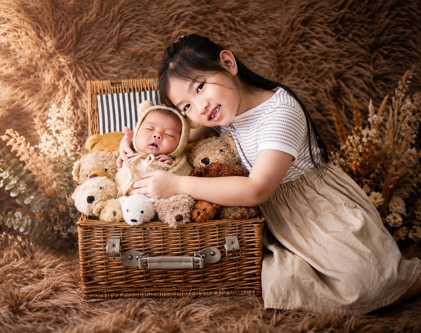 Young girl smiles proudly beside her newborn sibling nestled among teddy bears in a wicker basket.