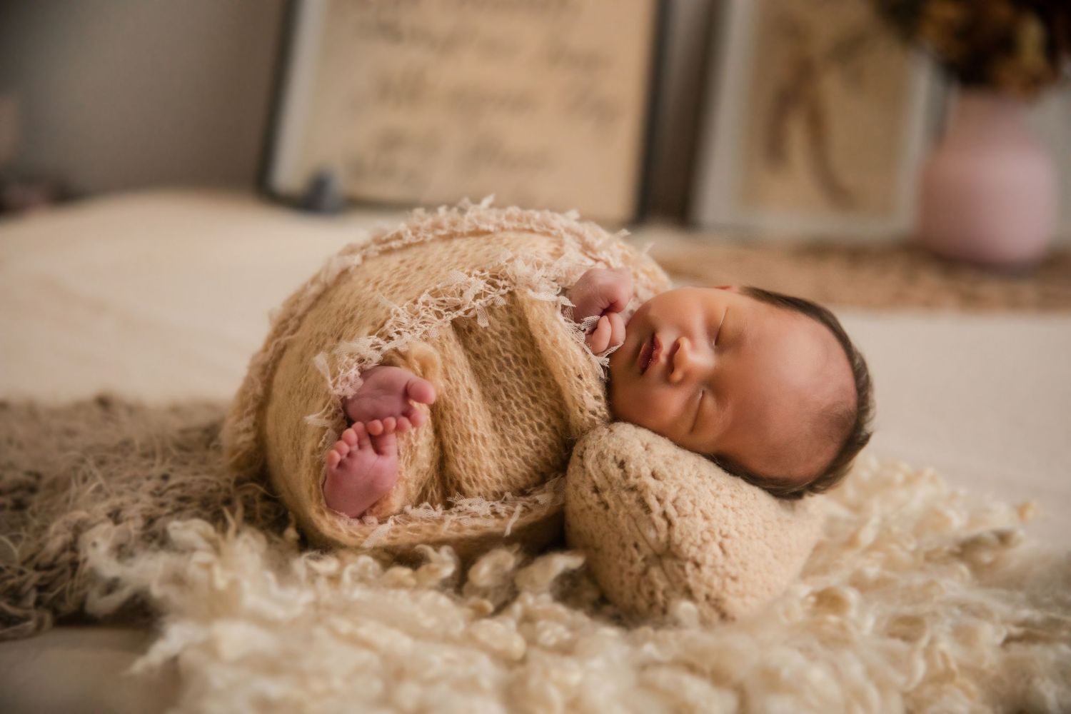 Newborn baby wrapped in a cozy beige knit swaddle, peacefully sleeping on a soft cream fur blanket.