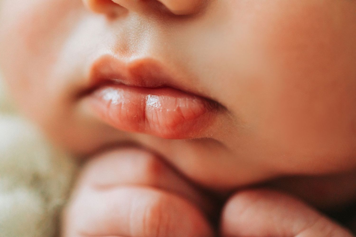 Close-up of a newborn baby's lips and chin, with tiny fingers resting gently beneath their face.