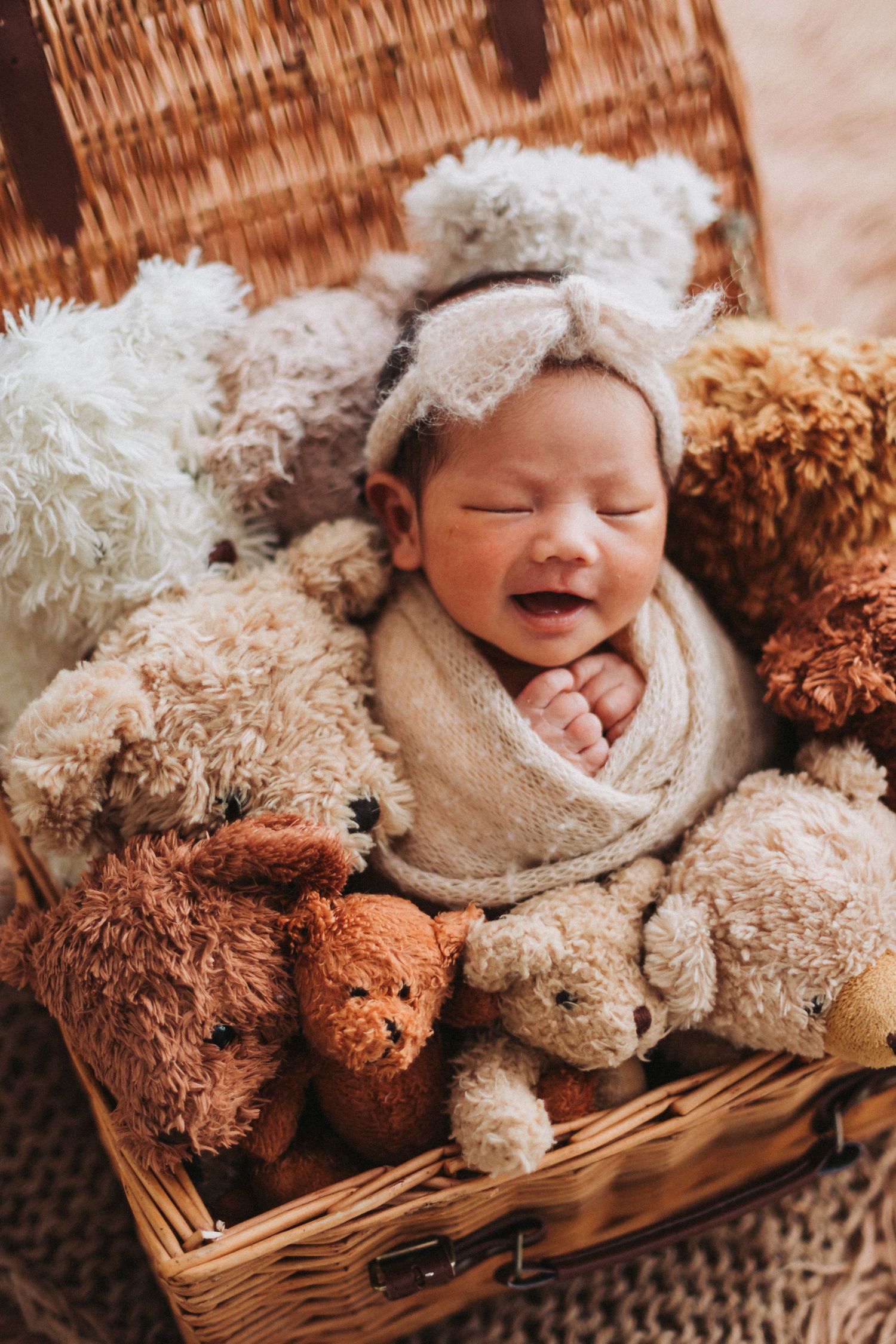 Newborn baby sleeping peacefully in a wicker basket surrounded by soft teddy bears, wearing a cozy bear ear bonnet.