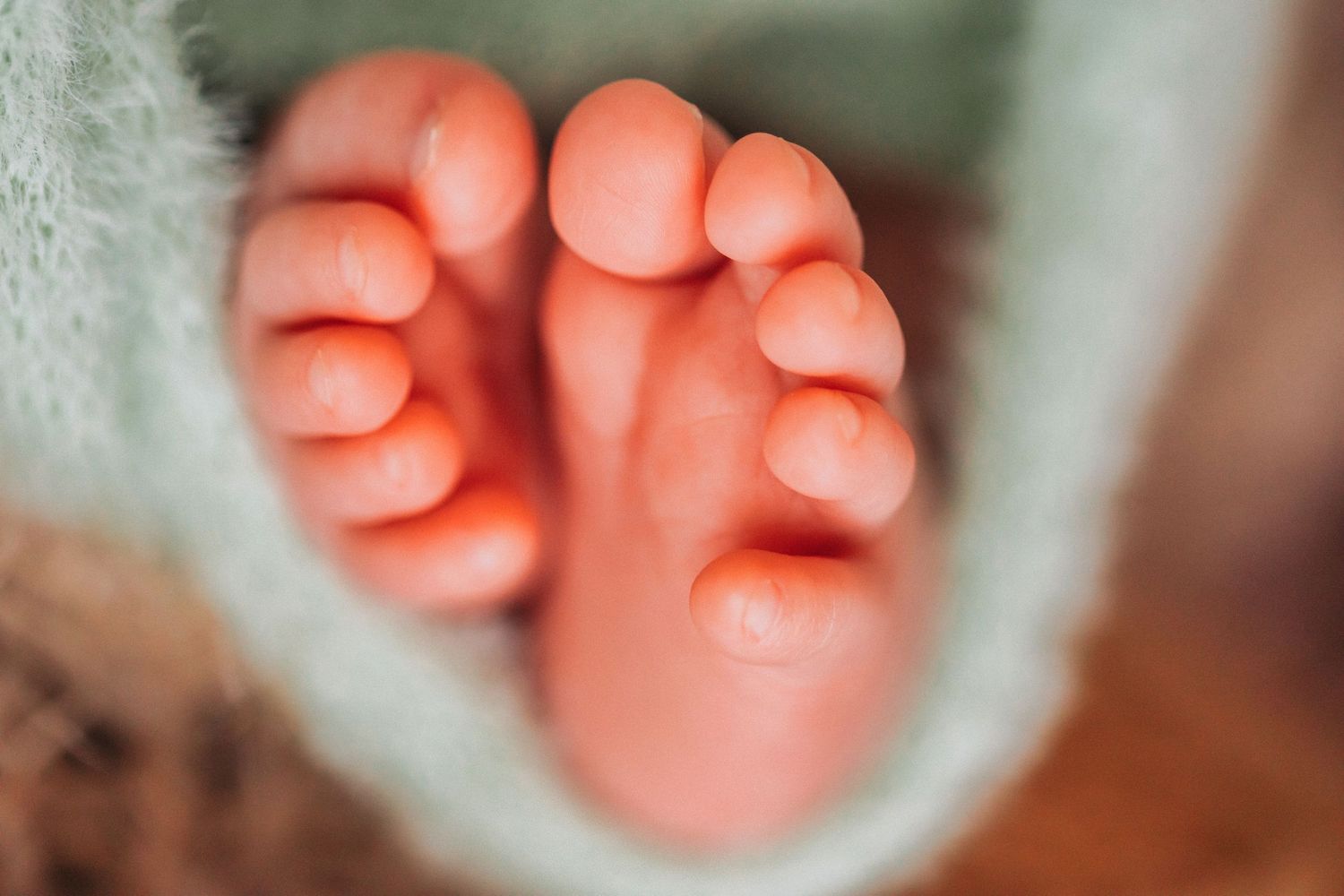 Close-up of tiny newborn baby feet wrapped in a soft mint green blanket, showcasing delicate pink toes.