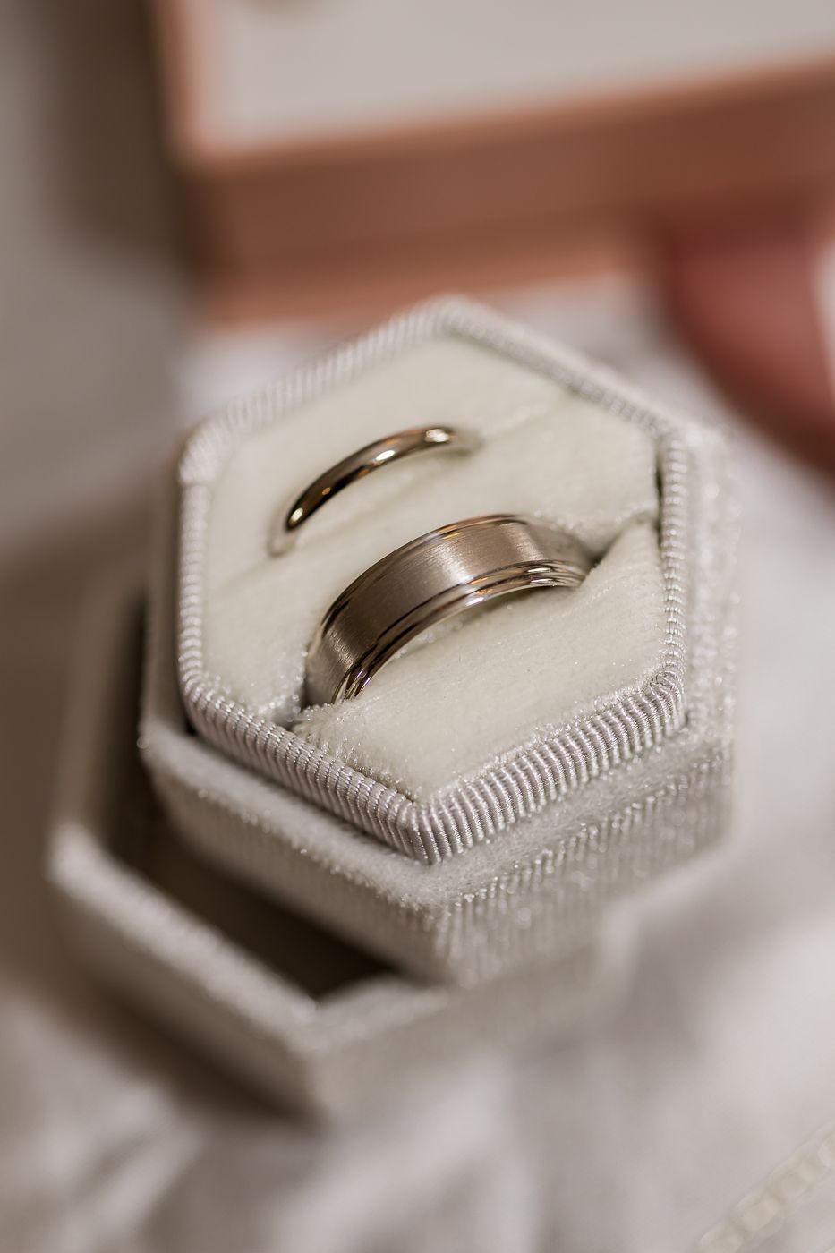 Two silver wedding bands displayed in a hexagonal ivory velvet ring box, symbolizing eternal love and commitment.