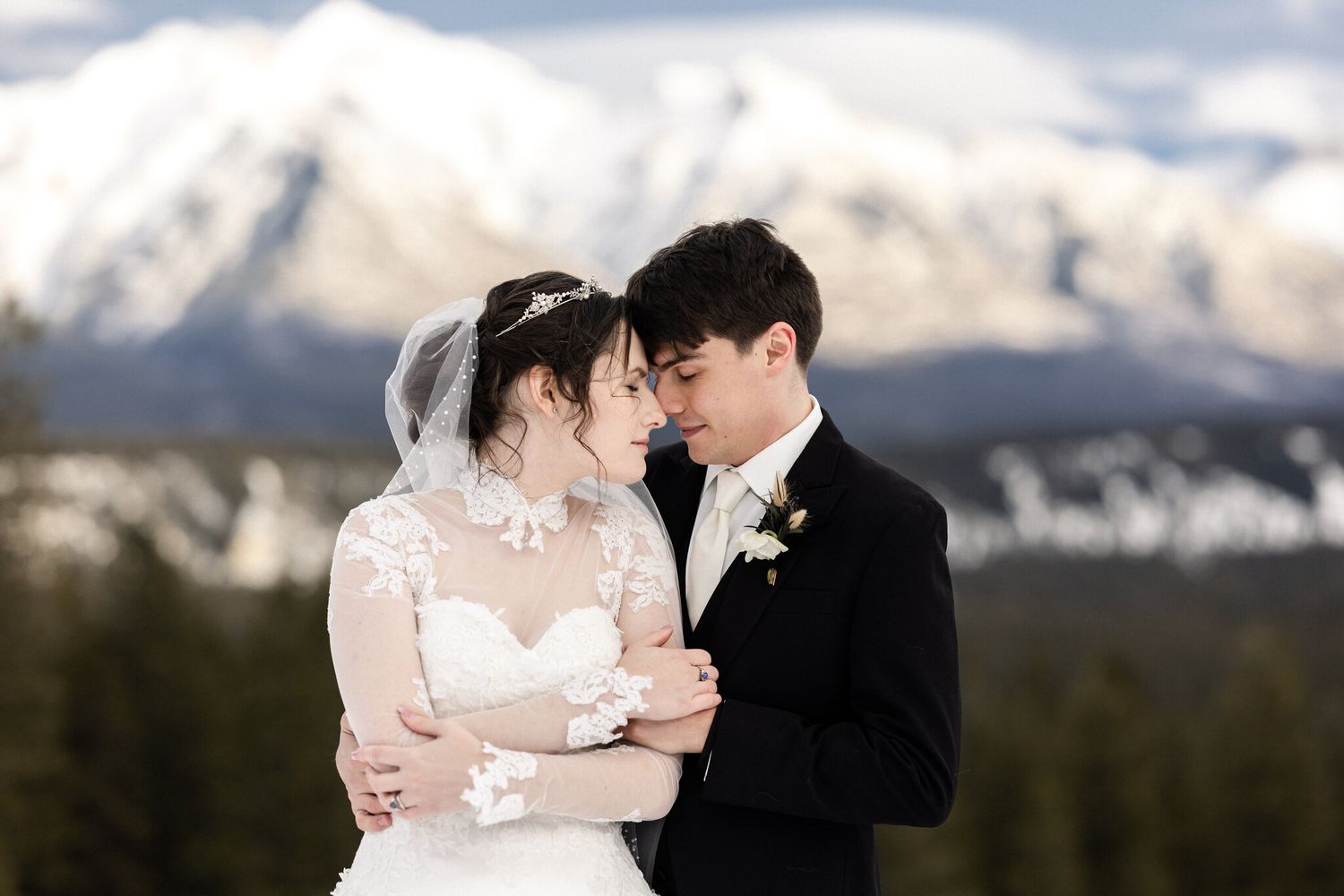 Bride and groom touching foreheads with snow-capped mountains behind, by a Calgary wedding photographer in Banff