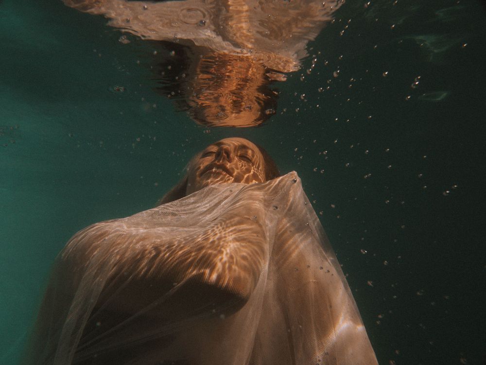 woman in a comforting pose underwater with her reflection on the surface in the pool session with Dip In Workshop NSW