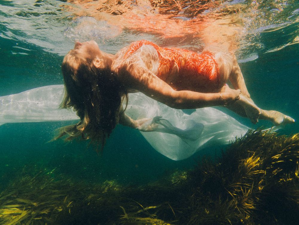 woman facing the surface of the water with seagrass floating around her underwater in the ocean at Lake Macquarie, NSW