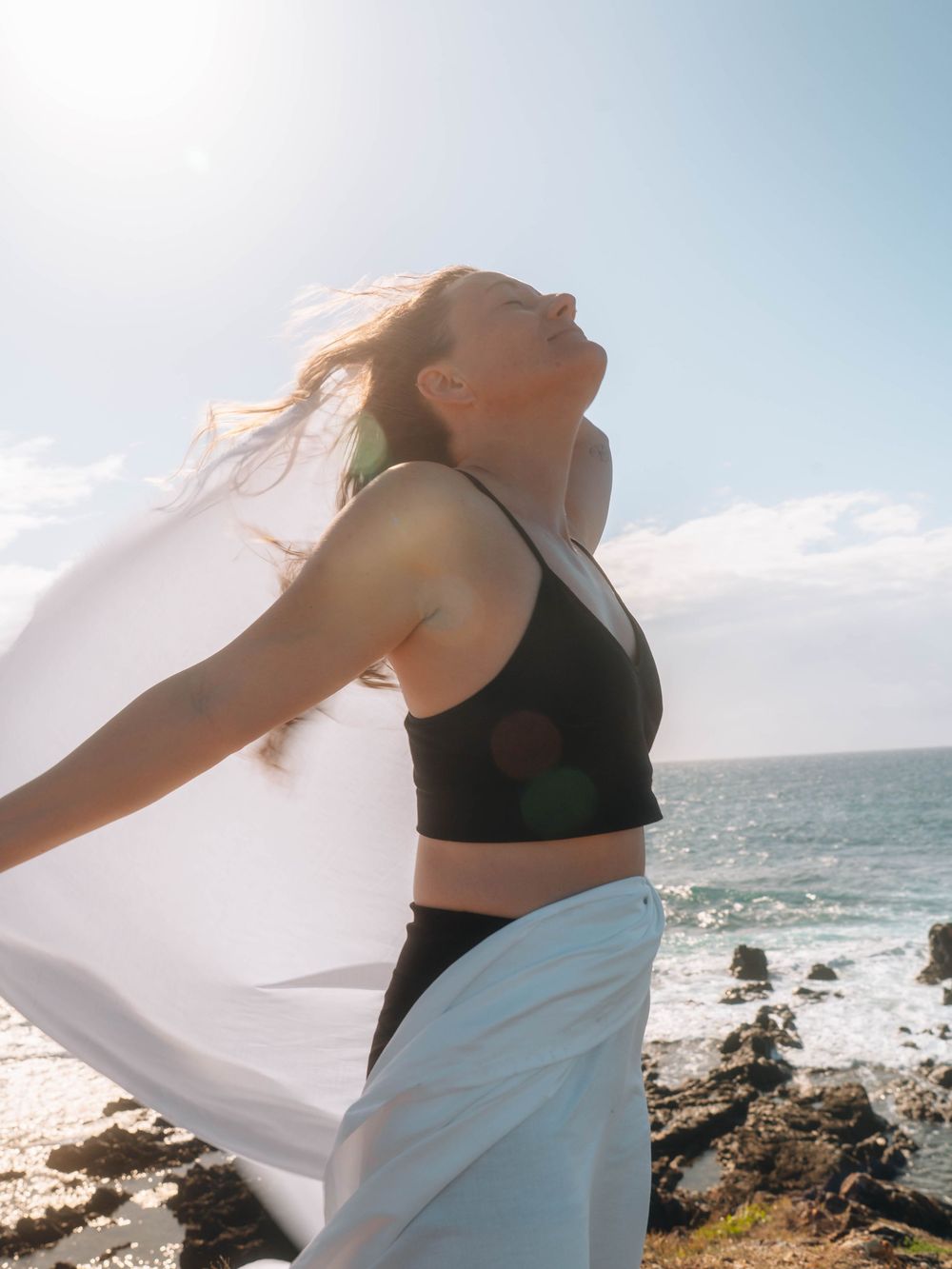 woman in an empowering freeing pose standing over the ocean edge in The Tide of Her portrait session