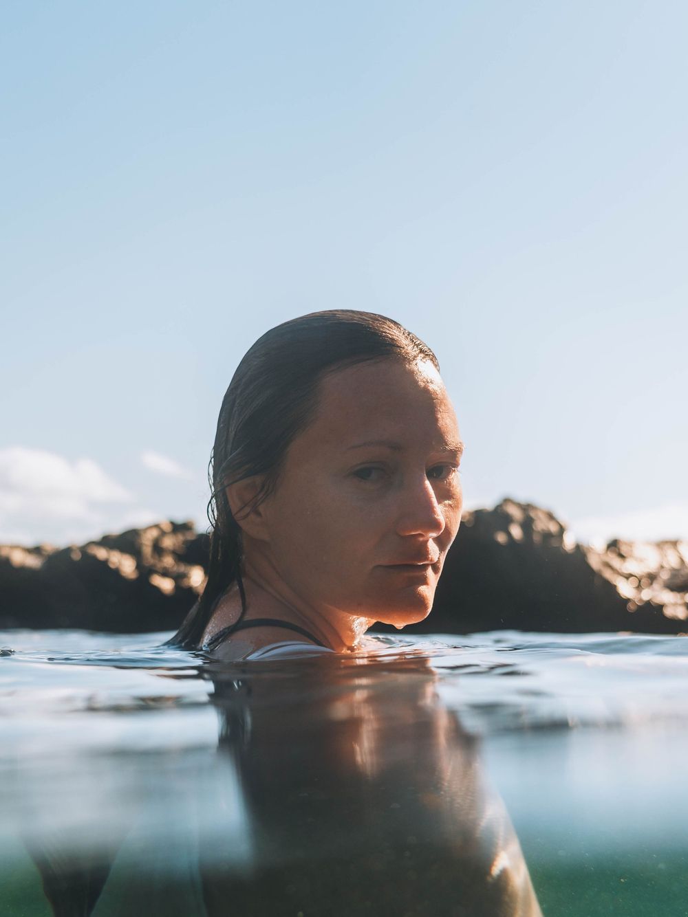 woman looking back into the lens with reflection of her face on water below during her first underwater portrait session in coastal NSW