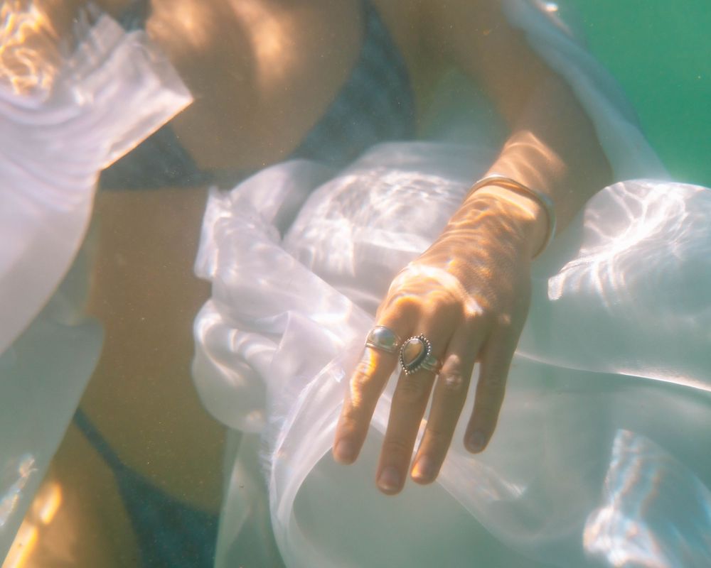 woman with ocean inspired jewellery on her hand underwater in reflective light on The Tide of Her portrait session in Lake Macquarie NSW