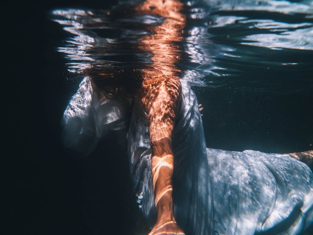 woman with ripples of water and light reflecting off her arm underwater in portrait session The Tide of Her with Kanari in coastal NSW