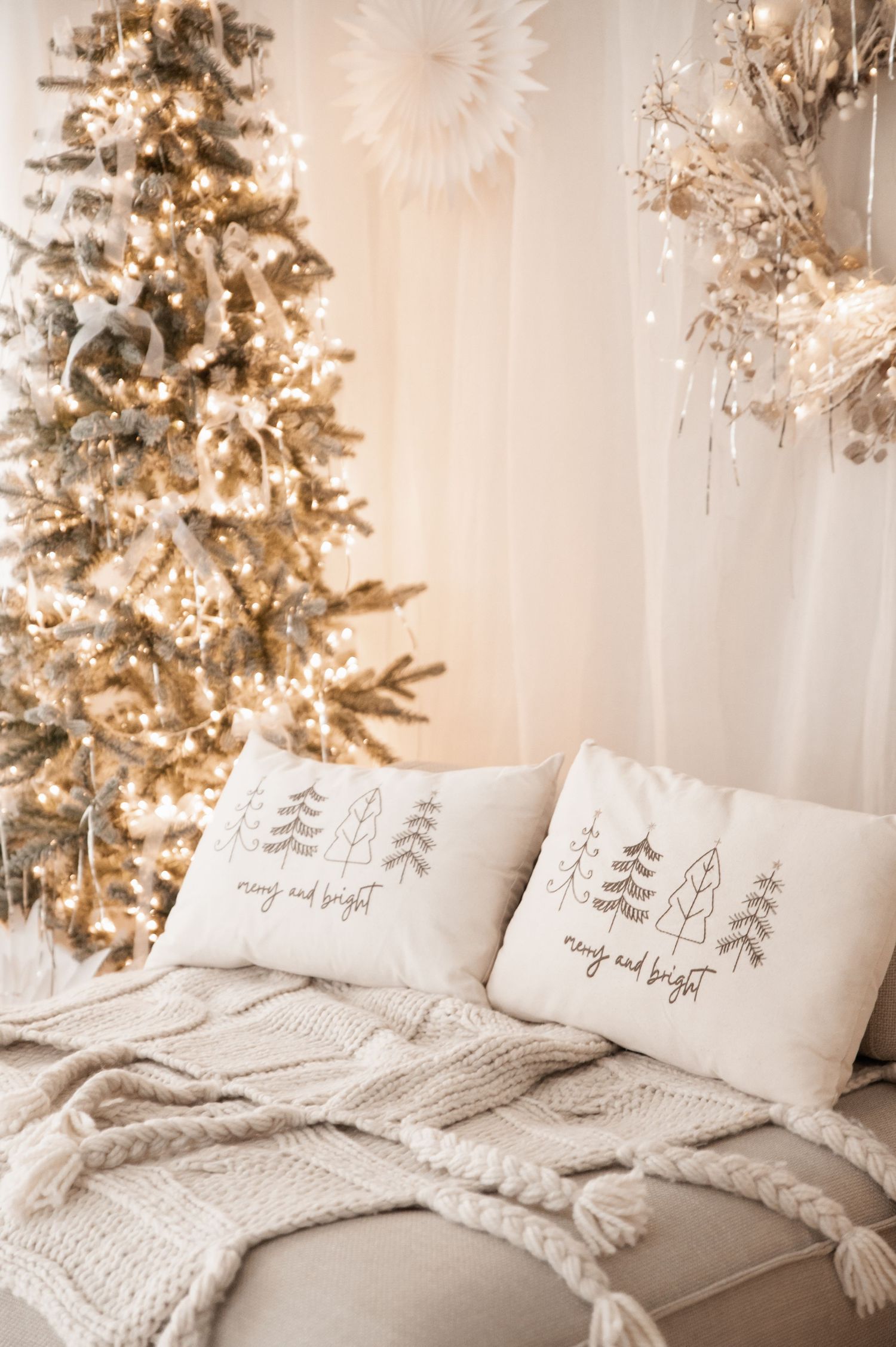 Cozy white Christmas bedroom with illuminated trees, textured bedding, and decorative winter-themed throw pillows.