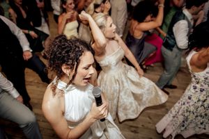 Women dancing and singing with microphone at lively wedding reception party celebration on wooden dance floor.