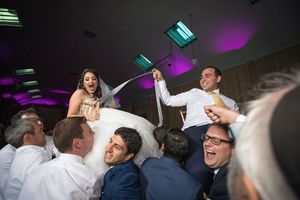 Bride and groom lifted by guests during joyful Jewish wedding hora dance celebration at elegant reception venue.
