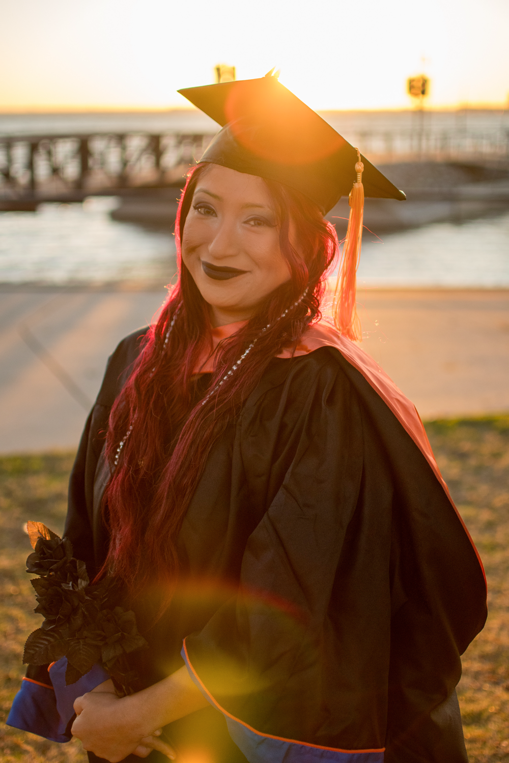 Graduate portrait wearing cap and gown on the doc at a lake