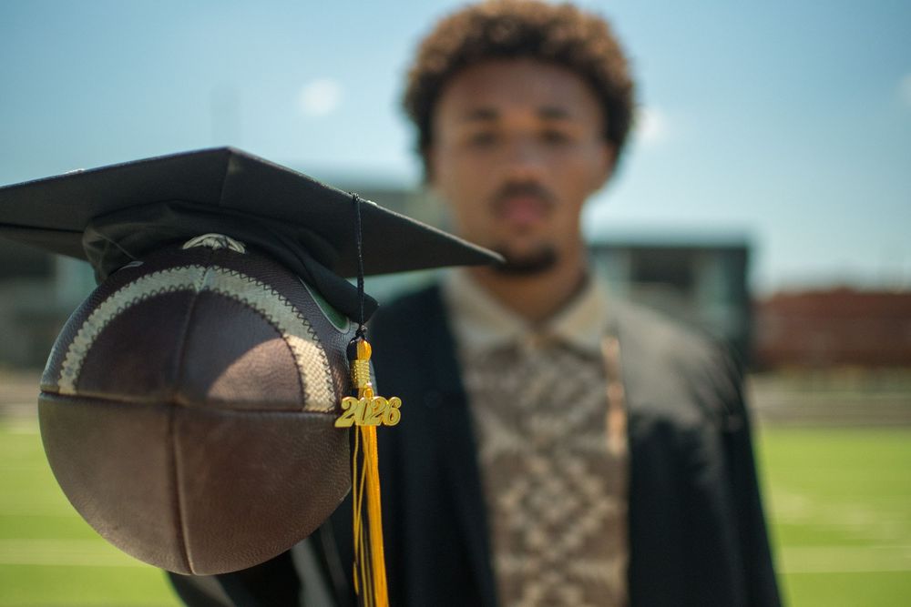 Senior graduation portrait featuring a graduation cap and football on the field