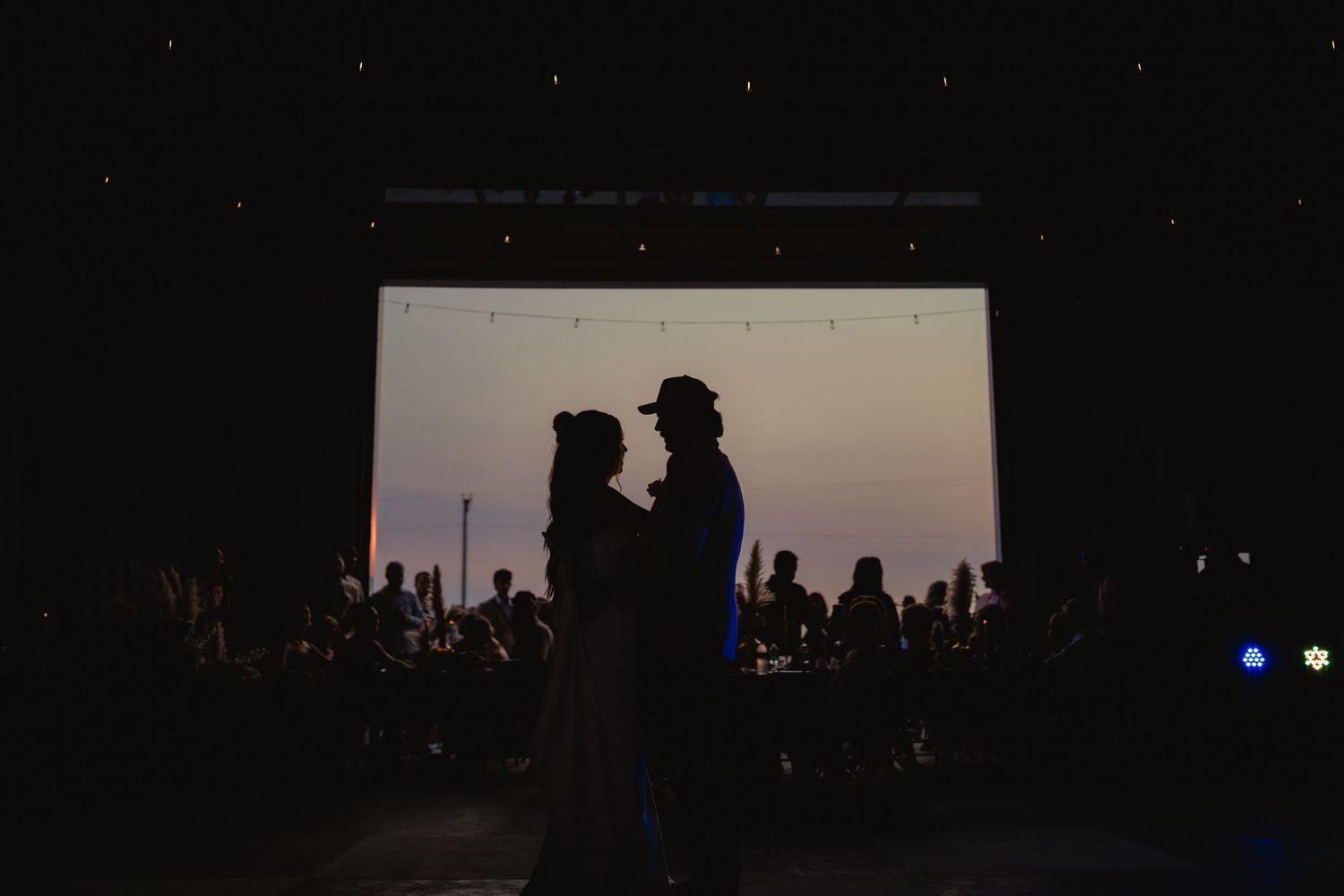 Silhouette of a couple sharing a first dance at a wedding reception with a glowing screen backdrop.