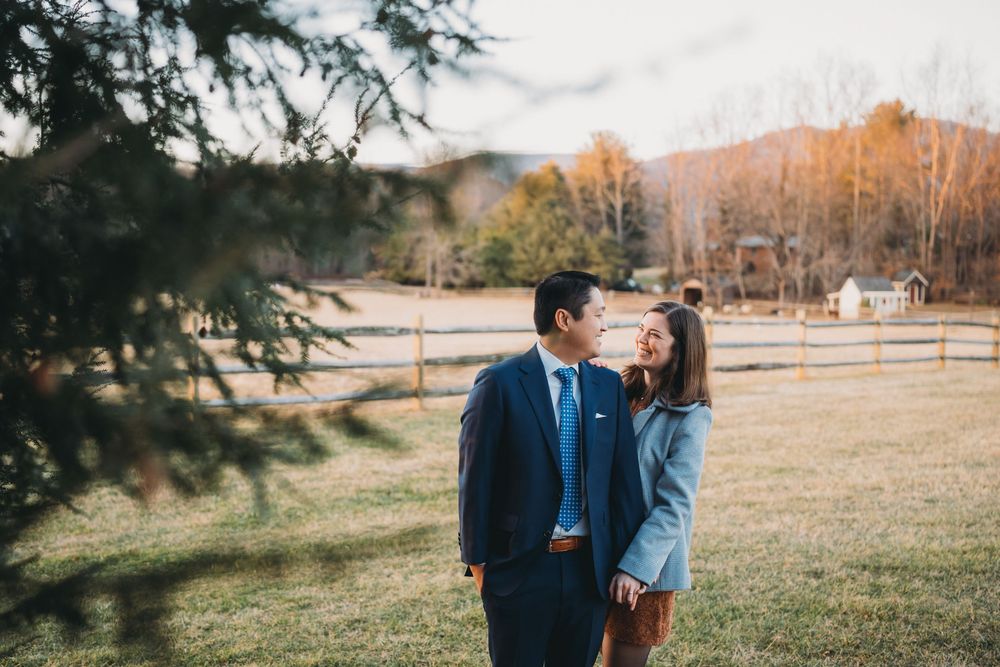 Couple sharing a romantic moment in a sunlit field with a wooden fence and mountains in the background at inn at little washington