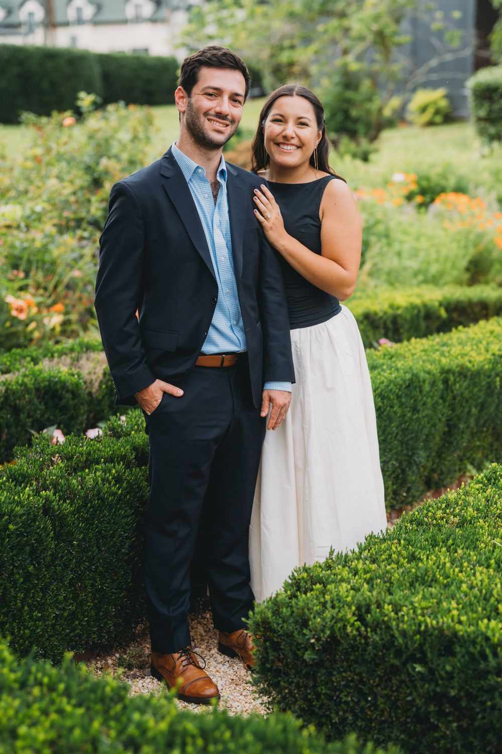 Couple posing in a formal garden, man in navy suit, woman in black top and white skirt, surrounded by hedges inn at little washington